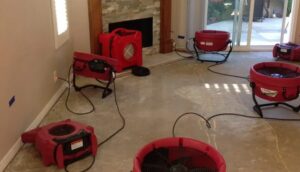 Multiple red industrial fans are actively drying a room's concrete floor after water damage