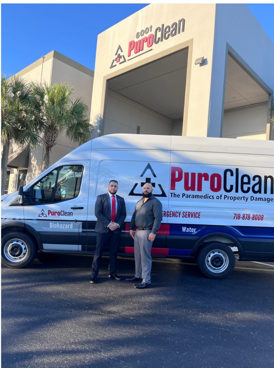 Two men stand proudly by a PuroClean service van with the company building behind them.