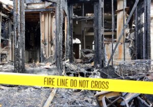 A charred house interior with burnt furniture and debris is cordoned off by yellow 'FIRE