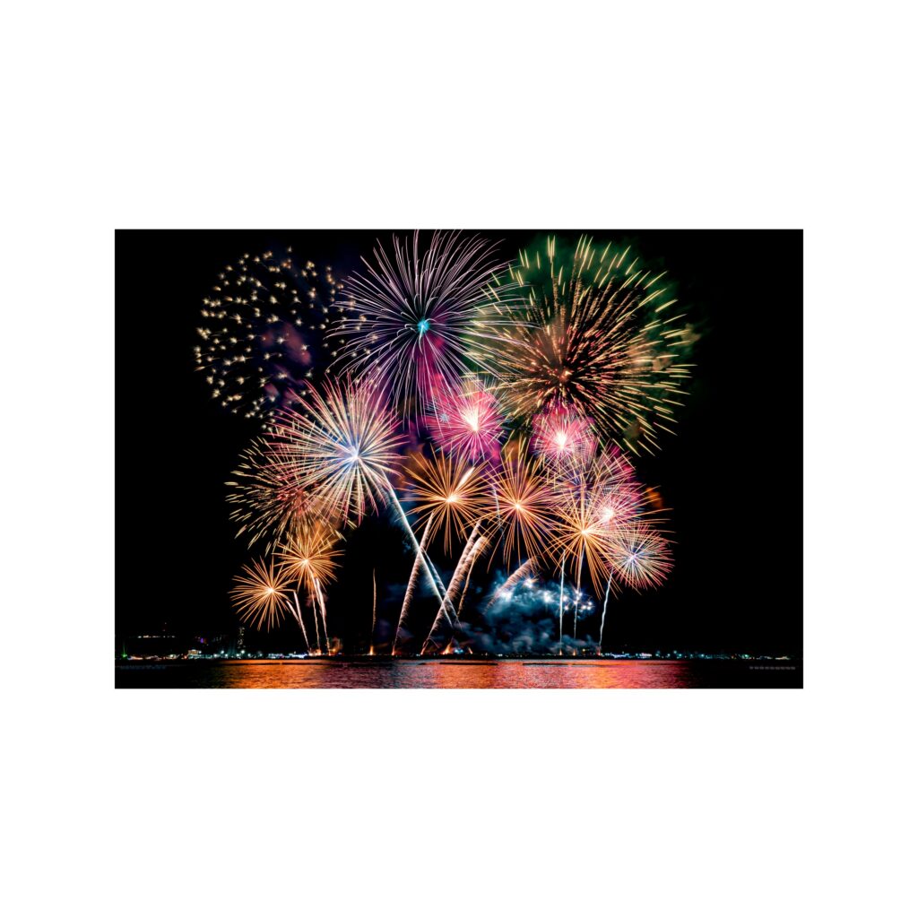 A spectacular display of colorful fireworks illuminates the night sky above a reflective body of water. TITLE