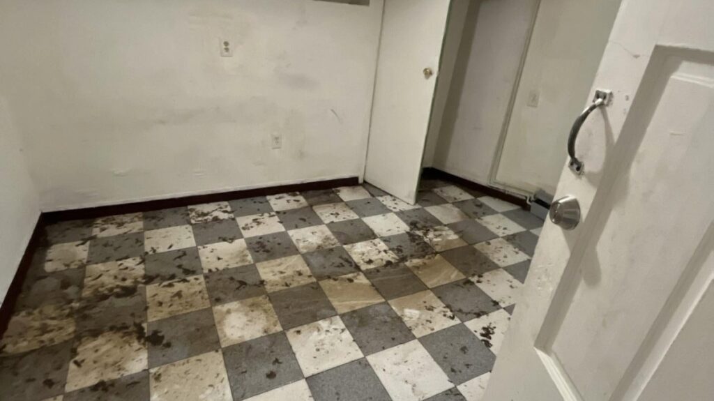 A neglected room with dirty, stained walls and a muddy checkerboard floor.