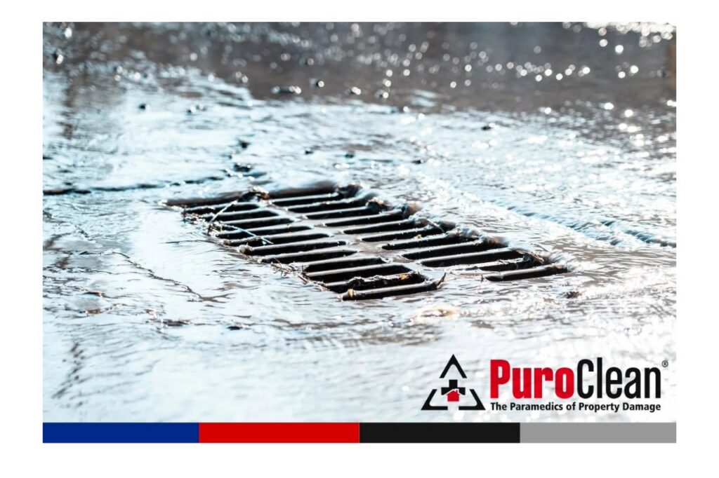 Rapidly flowing water rushes into a street storm drain, suggesting a drainage issue. TITLE