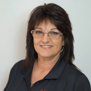 A smiling woman with dark hair and glasses wears a black PuroClean polo shirt.