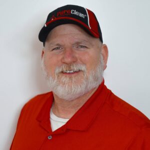 A friendly, bearded man in a PuroClean hat and red polo shirt smiles at the camera