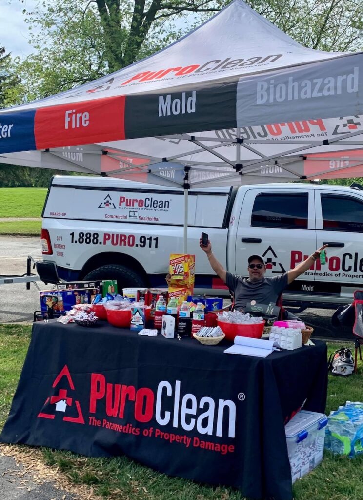 PuroClean booth set up with goodies and information. Man sitting at table to raise awareness.