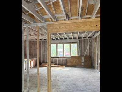 Framed interior of a residential property undergoing code compliant reconstruction, showcasing new structural beams, updated insulation space, and open ceiling joists in compliance with modern building codes.