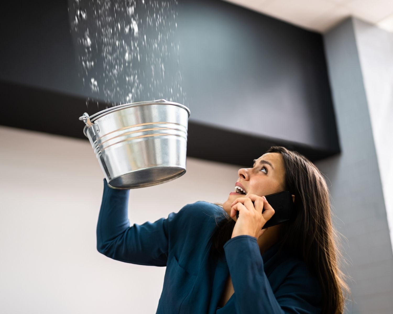 Woman using bucket to catch water from ceiling leak during winter storm