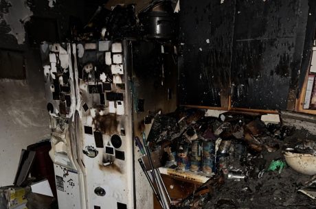 Fire-damaged kitchen with smoke-stained refrigerator, charred cabinets, and heavy soot and debris after an electrical fire.