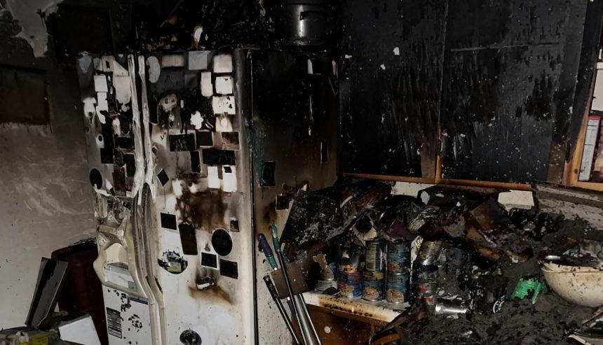 Fire-damaged kitchen with smoke-stained refrigerator, charred cabinets, and heavy soot and debris after an electrical fire.