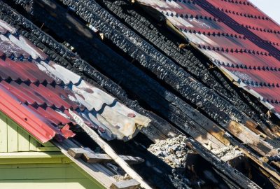 Charred wooden roof beams beneath damaged metal roofing after house fire