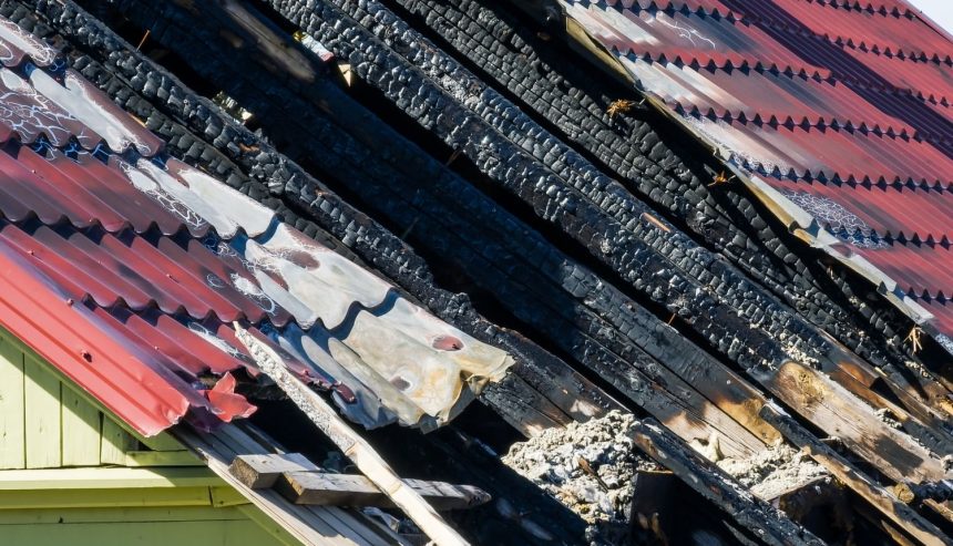 Charred wooden roof beams beneath damaged metal roofing after house fire