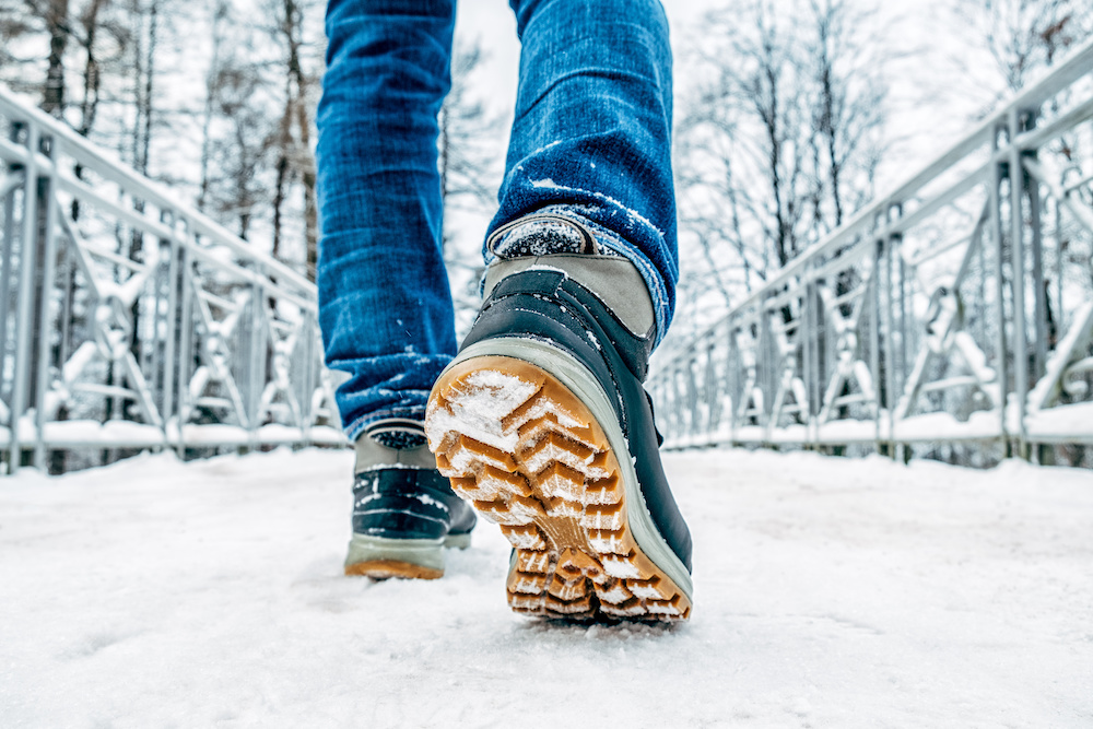 Man's legs in black with orange boots walking in the snow. Winter safety tips.