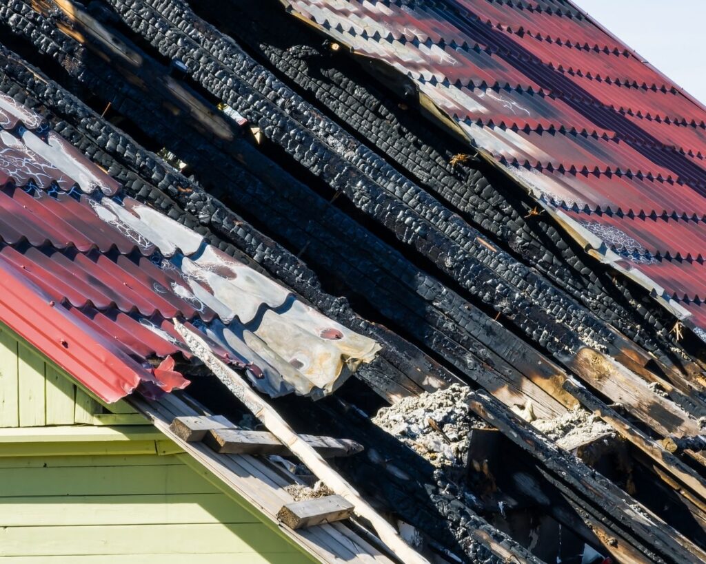 Charred wooden roof beams beneath damaged metal roofing after house fire