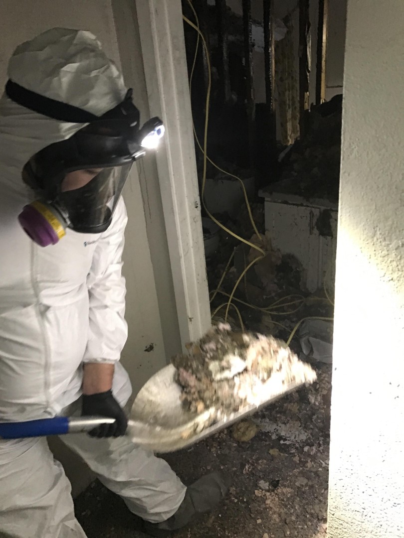 Respirator-equipped technician shoveling fire debris during cleanup in a Woodinville WA home