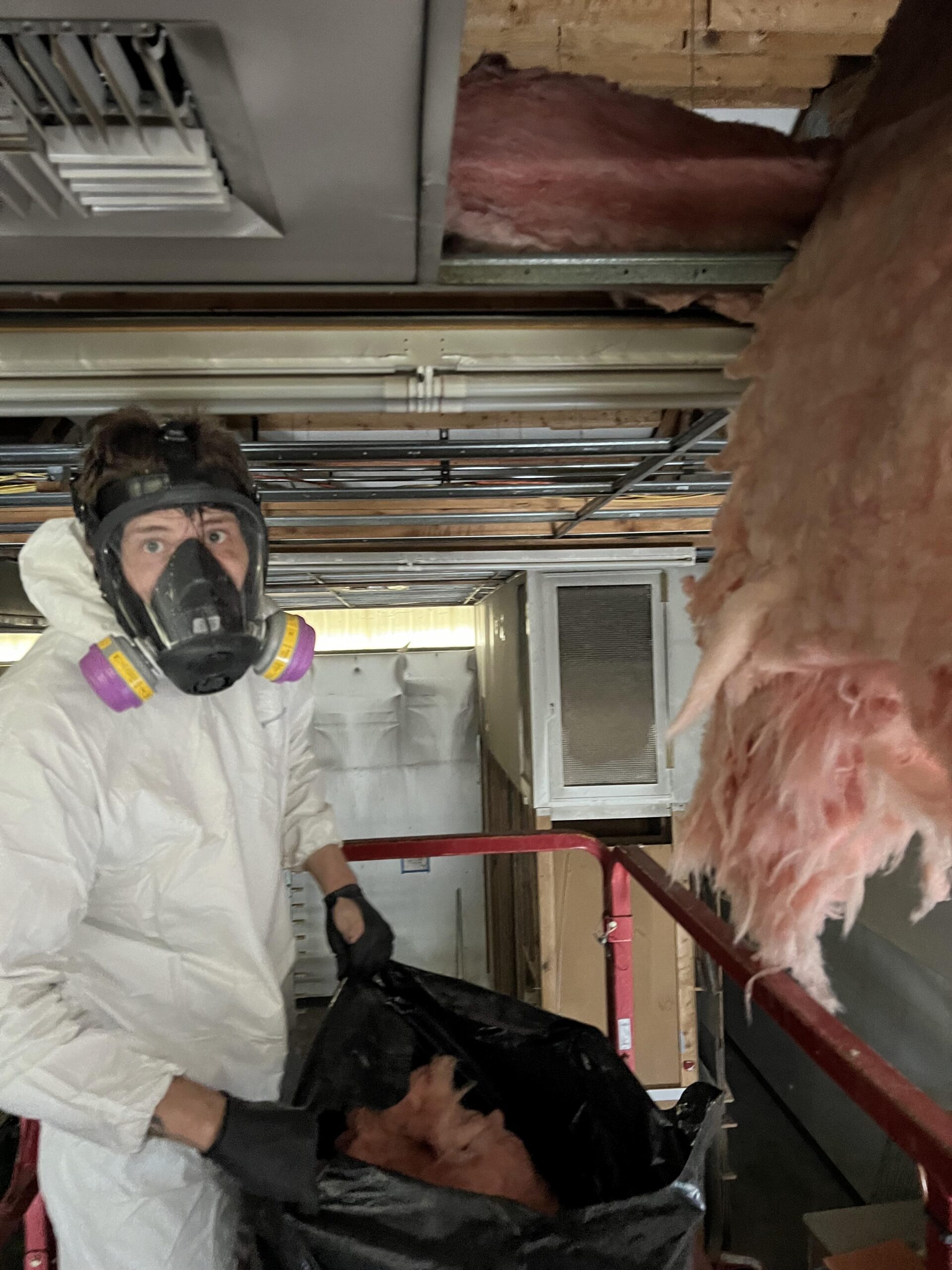 Restoration technician in PPE removing smoke saturated batt insulation from the ceiling of a Seattle WA commercial shop