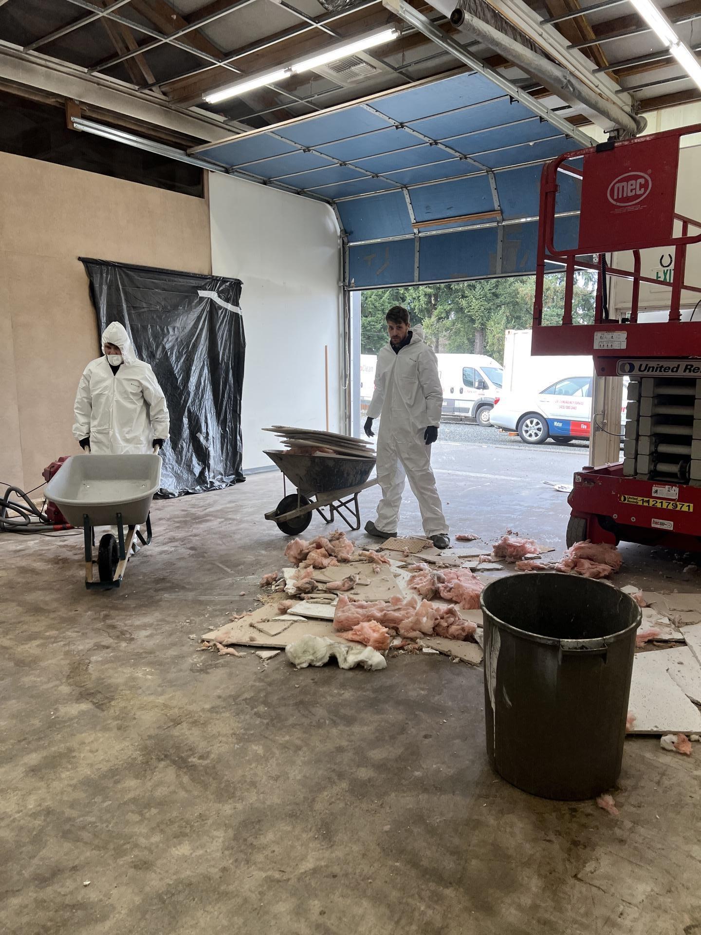 Restoration crew hauling wheelbarrow loads of fire damaged debris out of a commercial woodworking shop in Seattle WA