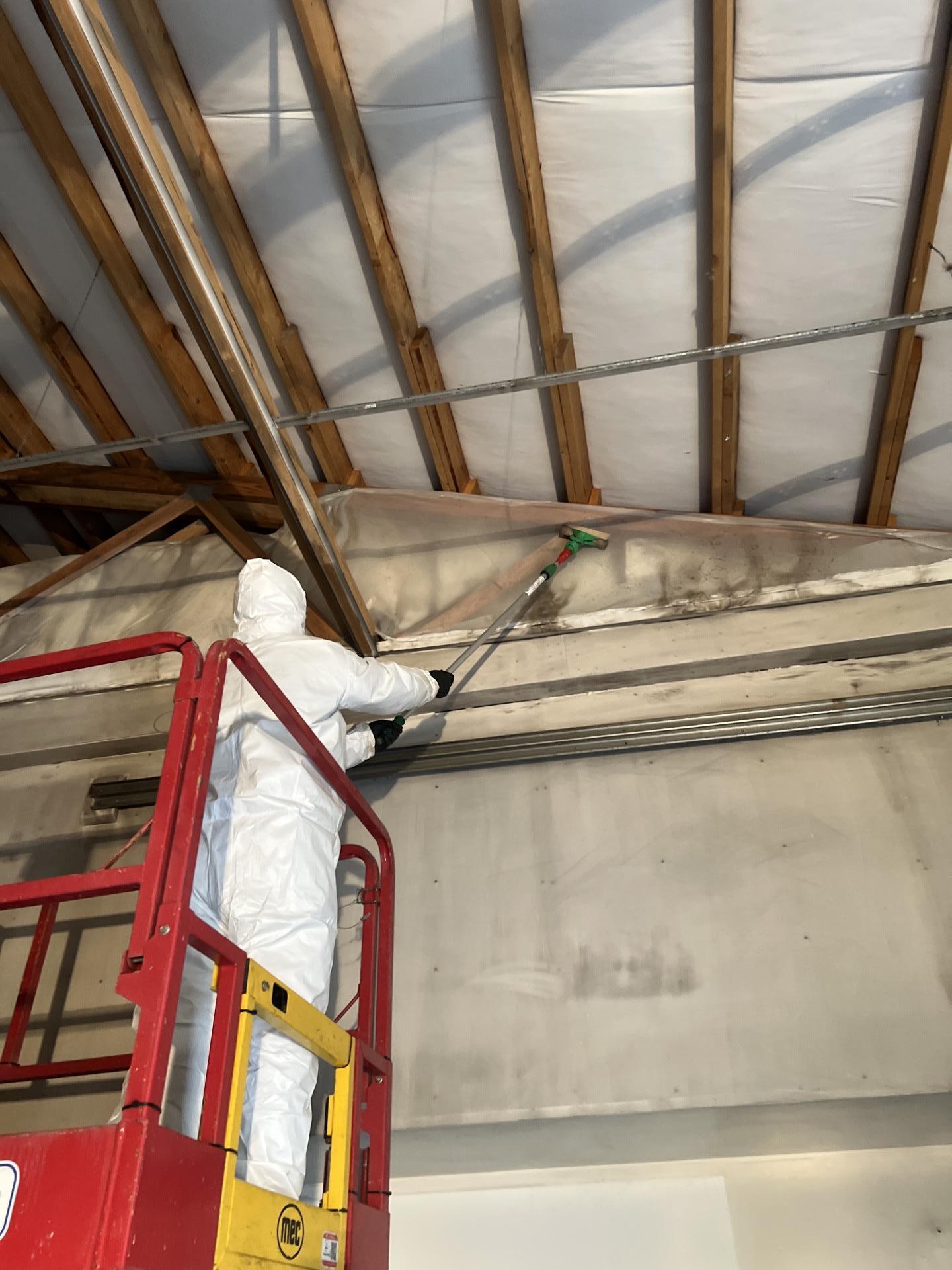 Technician cleaning soot from exposed ceiling structure and ductwork from a lift inside a Seattle WA commercial shop