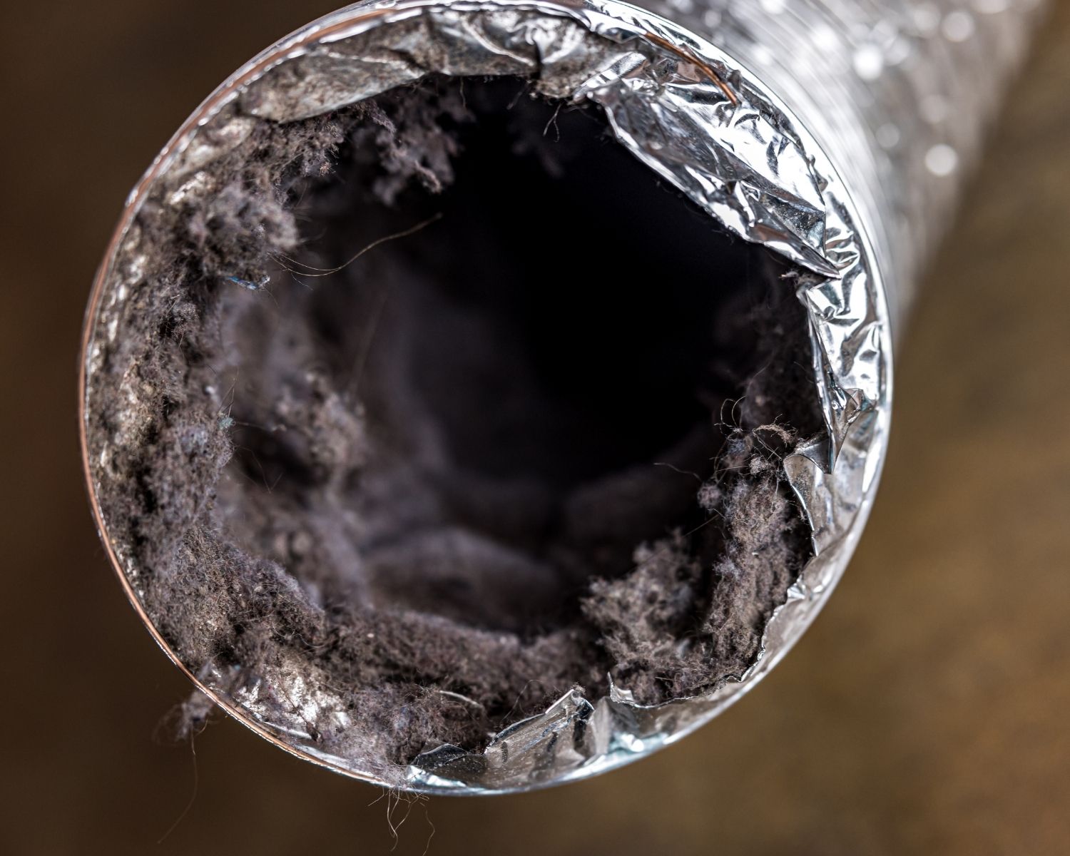 Interior of a flexible metal air duct packed with dark residue and buildup blocking the airflow