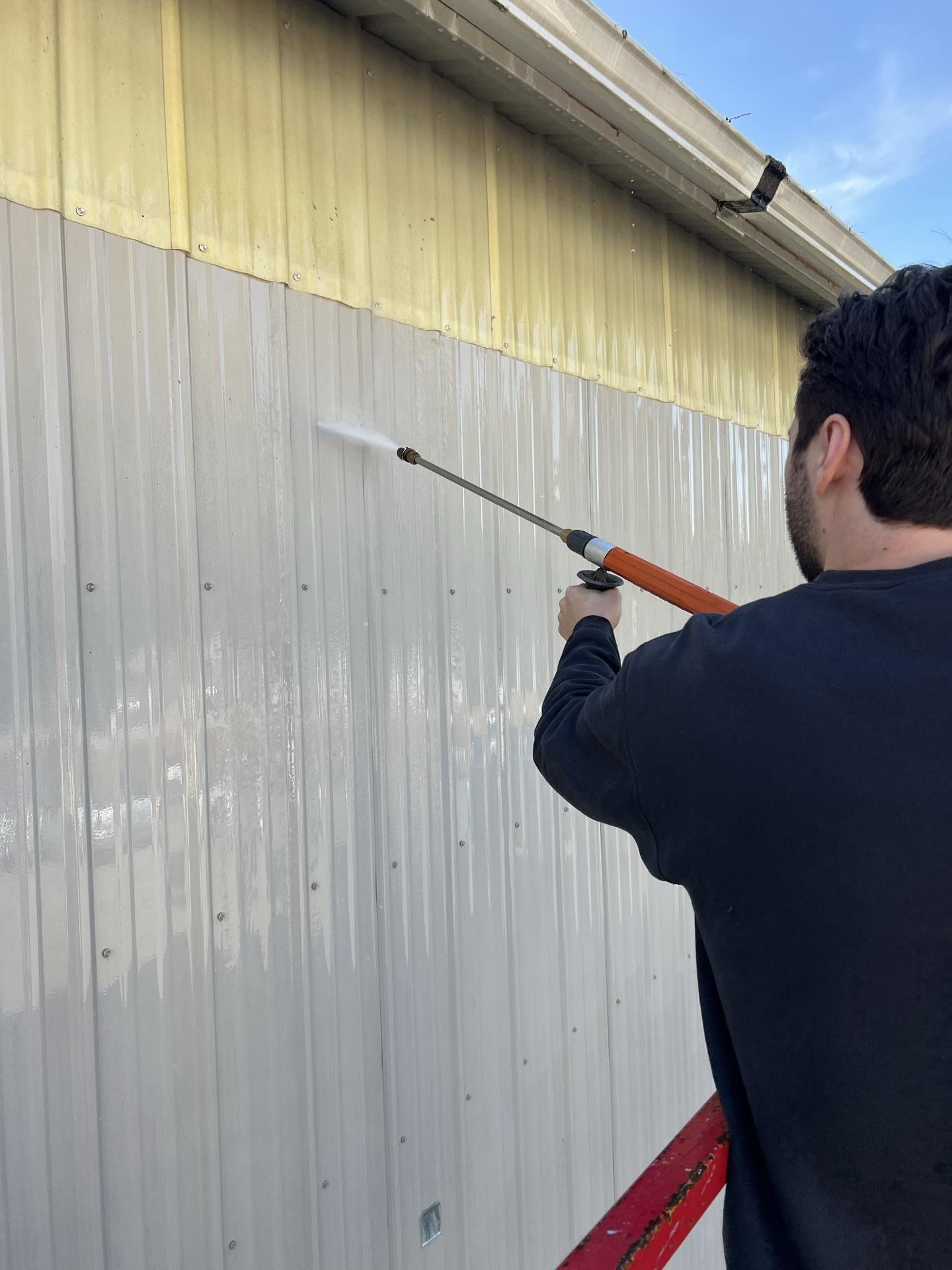 Technician pressure washing soot streaked metal siding on the exterior of a fire damaged Seattle WA commercial shop