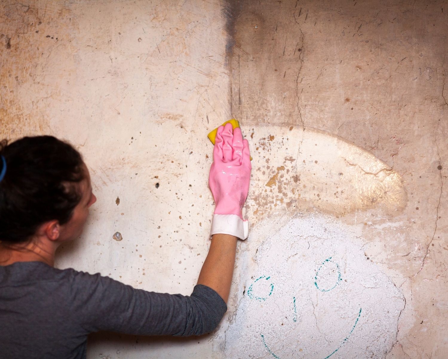 Gloved hand wiping soot staining off an interior wall with a sponge, leaving a clean streak behind