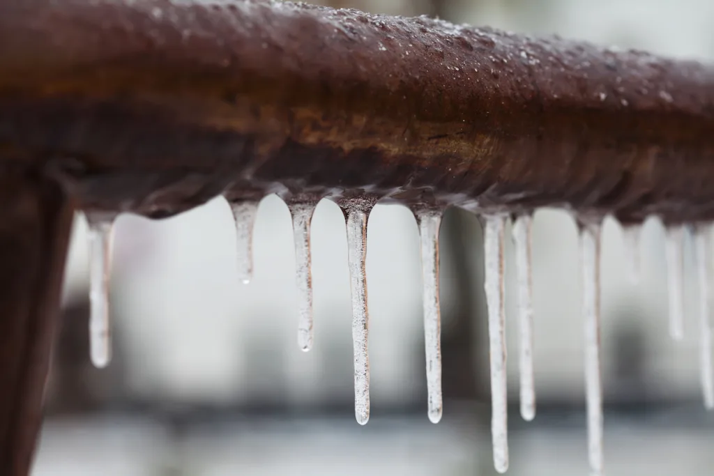 Icicles hanging from a frozen, rusty pipe, illustrating