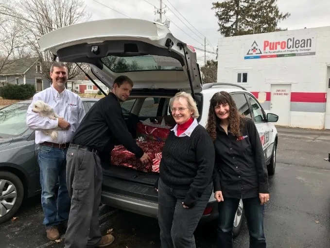 PuroClean team members load holiday gifts into a car, smiling and engaging in community service.