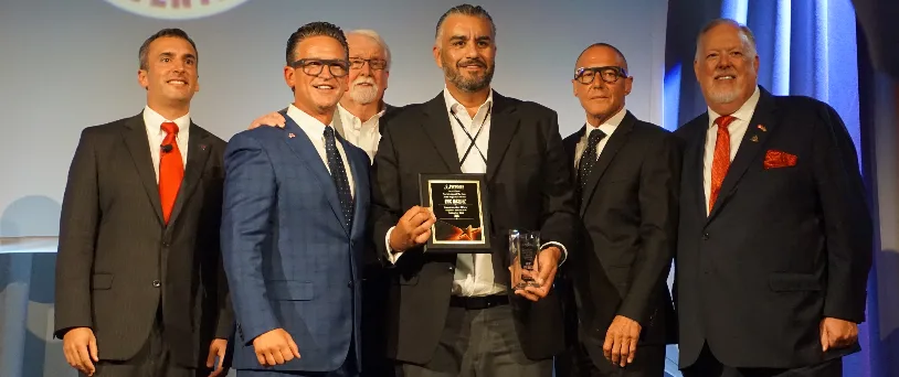 A group of five men at an award ceremony, with one man holding the Technician of the Year plaque.