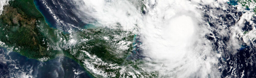 Satellite view of a hurricane approaching Central America, with swirling clouds and land visible below.