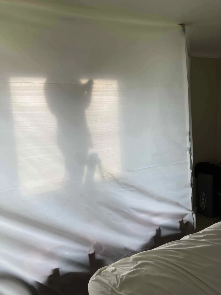 White plastic sheeting covers a wall with shadows of a person and