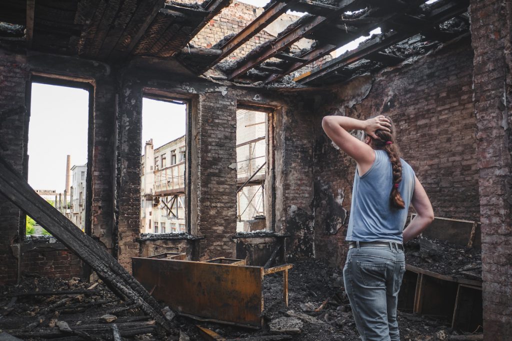 A sad man holds his head by hand and cries in a burnt-out house after the disaster.