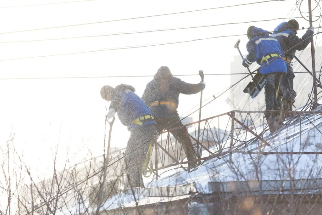 Four people in the crew wearing harnesses to remove snow.