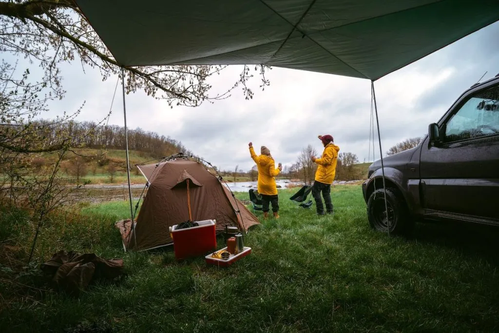 Two people camping outside near a lake with a camping tent.