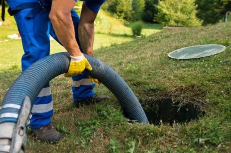 A man uses a hose to drain a septic tank in the ground