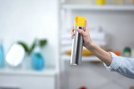 person with an odor removal spray can
