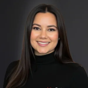 A smiling woman with long dark hair wearing a black turtleneck against a dark background.