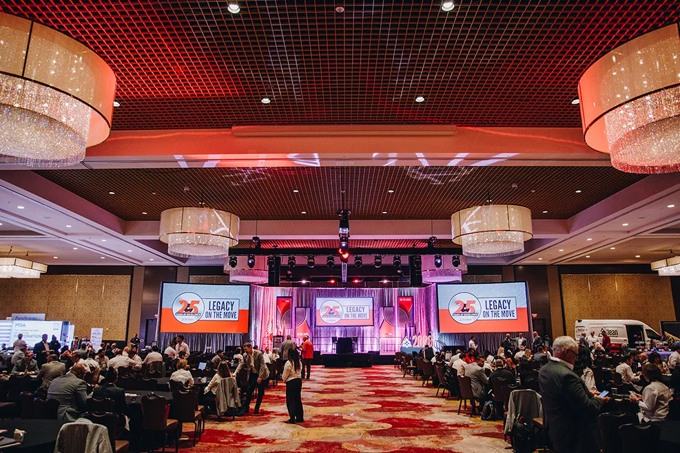 Attendees gather in a grand ballroom featuring a stage with screens displaying