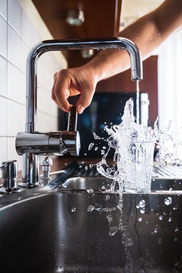 Frozen pipes and warm weather - person filling up cup with water from faucet