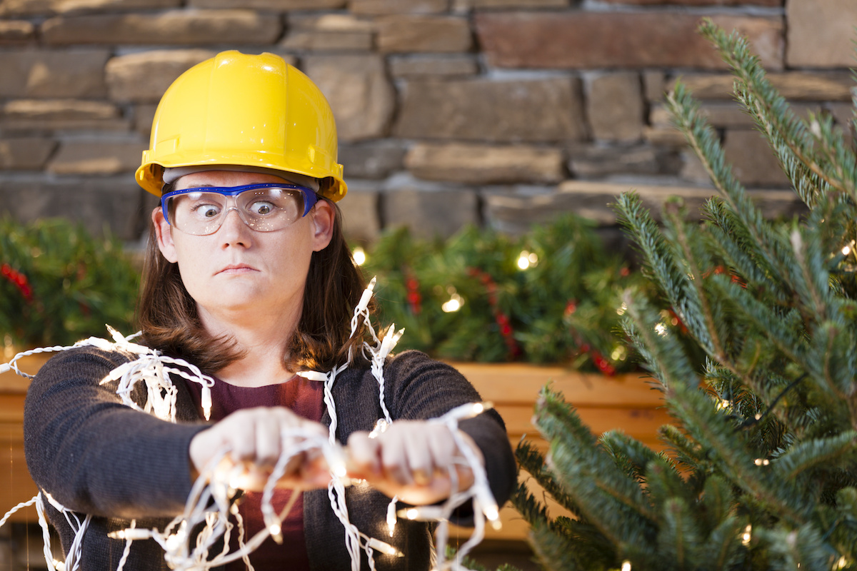 Woman plugging in Christmas lights with hard hat on after following holiday safety tips